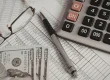 Calculator, financial documents, and US dollar bills representing accounting, payroll, and business finance management
