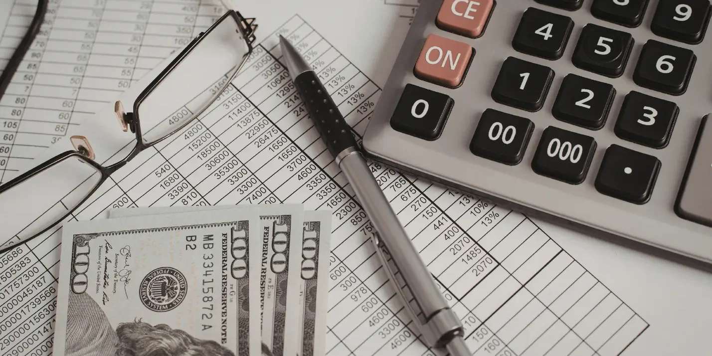 Calculator, financial documents, and US dollar bills representing accounting, payroll, and business finance management