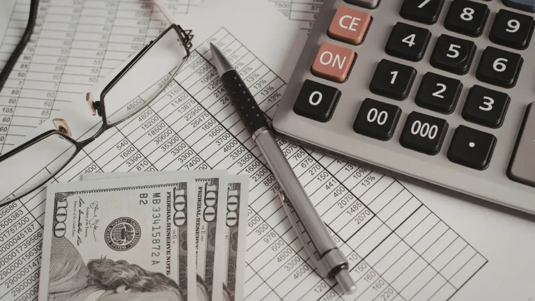 Calculator, financial documents, and US dollar bills representing accounting, payroll, and business finance management